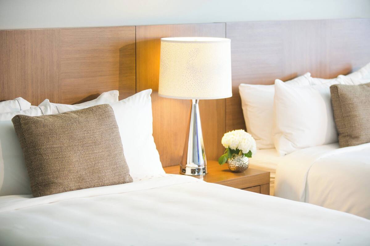 Une chambre d’hôtel avec un lit bien fait, une lampe de chevet et un petit vase avec des fleurs.