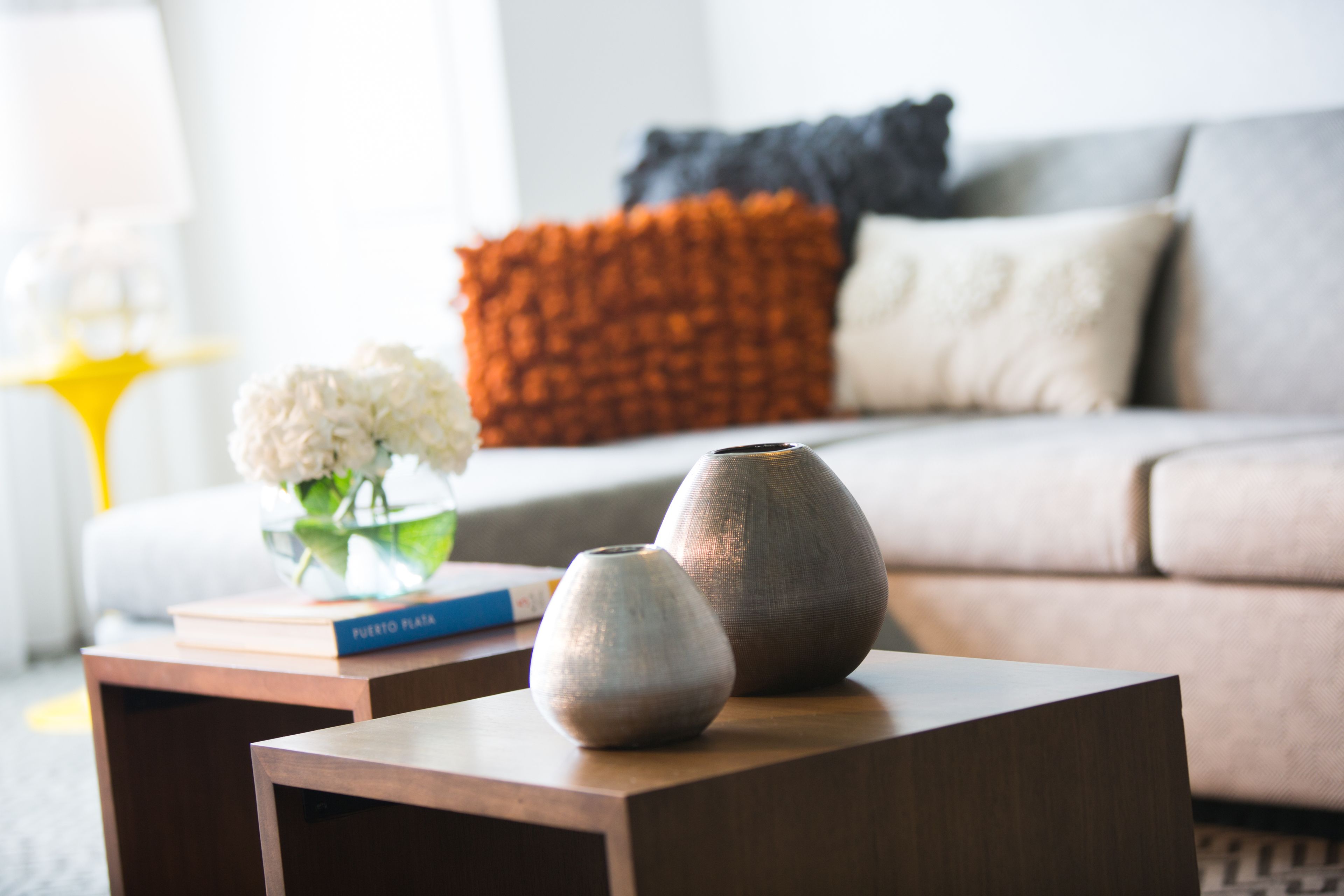 A modern living room with a sofa, decorative pillows, a small table with vases, and a book.