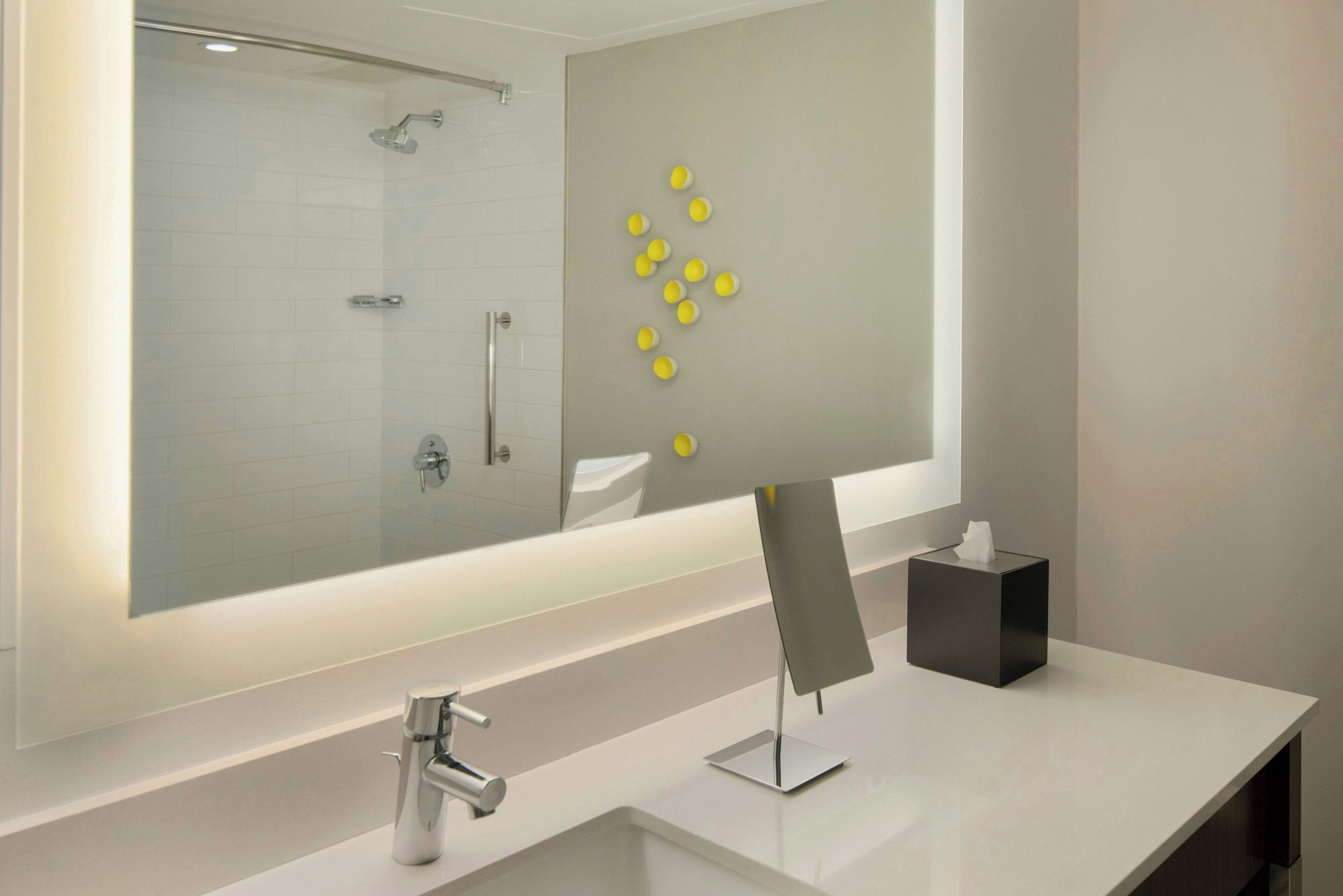 A modern bathroom with a large mirror, a white sink, and a glass-enclosed shower.