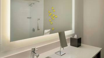 A modern bathroom with a large mirror, a white sink, and a glass-enclosed shower.