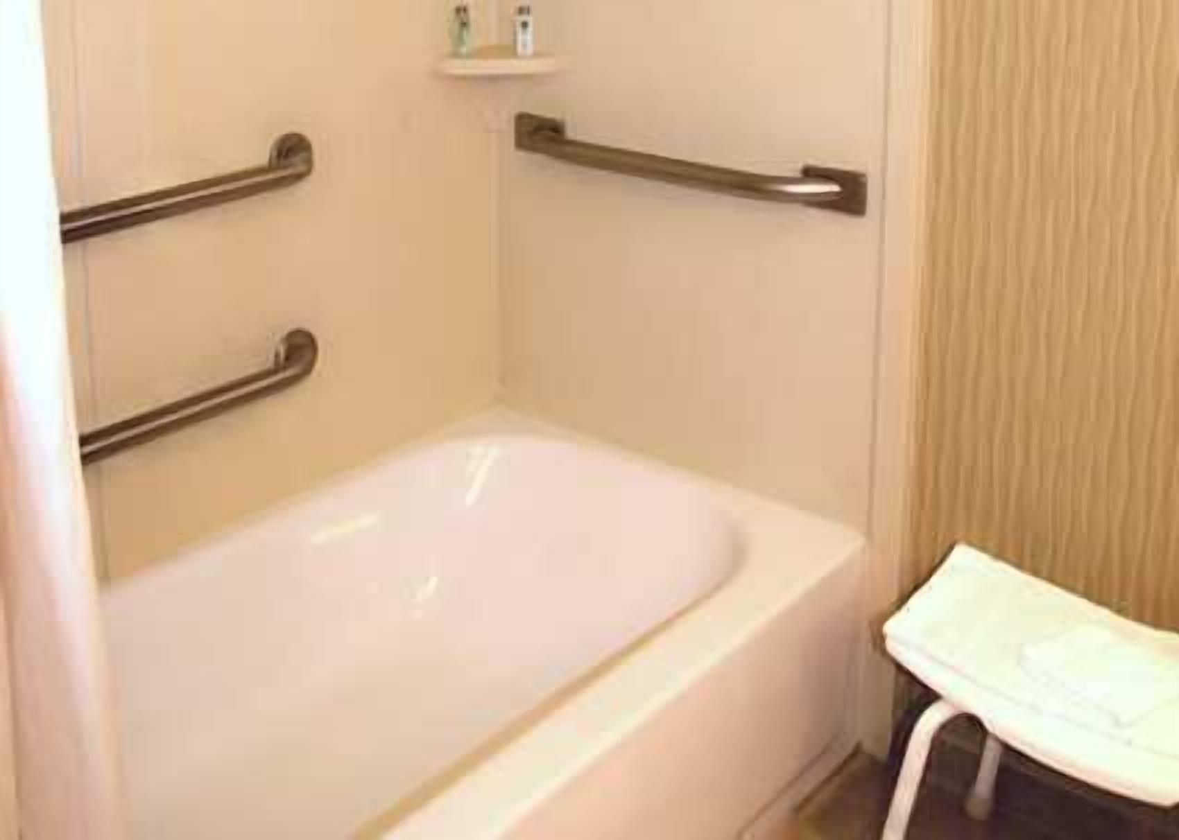 A bathroom with a white bathtub, a handrail, and a small shelf with toiletries.