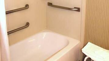 A bathroom with a white bathtub, a handrail, and a small shelf with toiletries.