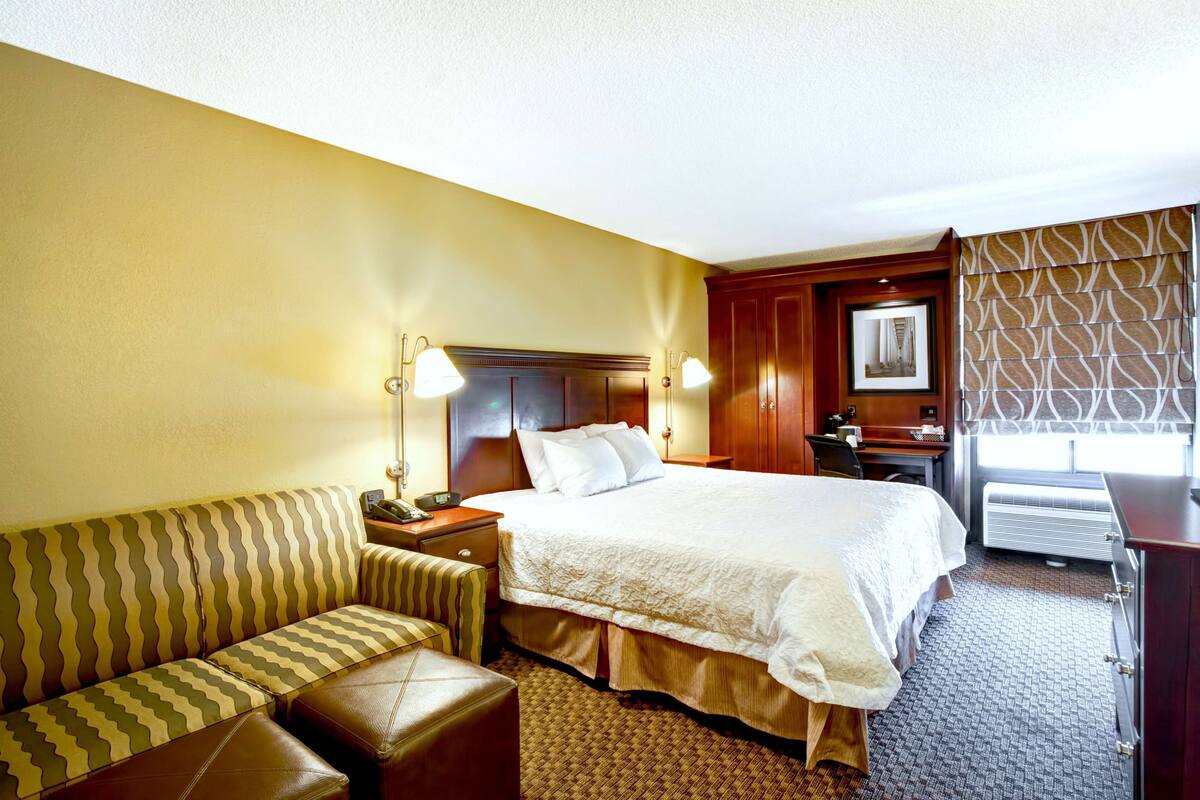 A hotel room with a bed, a sofa, a desk, and a window with patterned curtains.