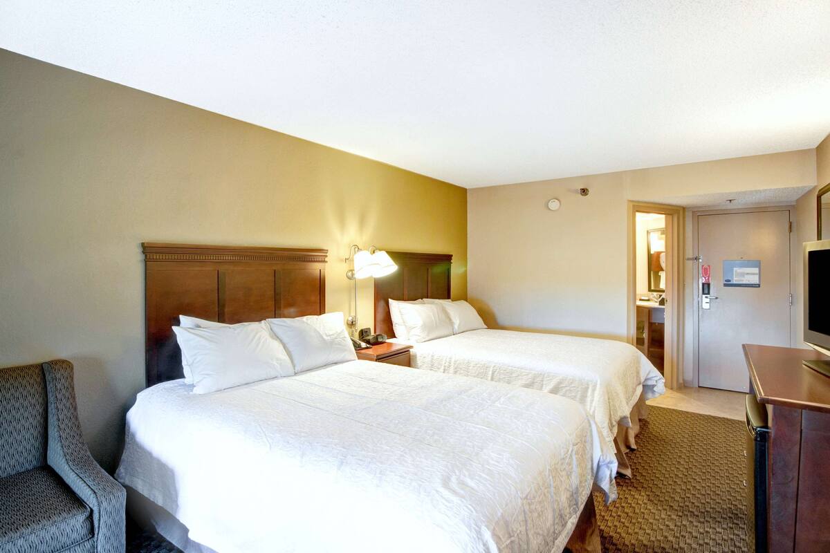 A hotel room with two beds, a desk, a chair, a television, and a door leading to a bathroom.