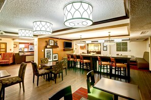 Un hall d’hôtel comprenant un bar, des espaces aménagés avec des sièges et un téléviseur.