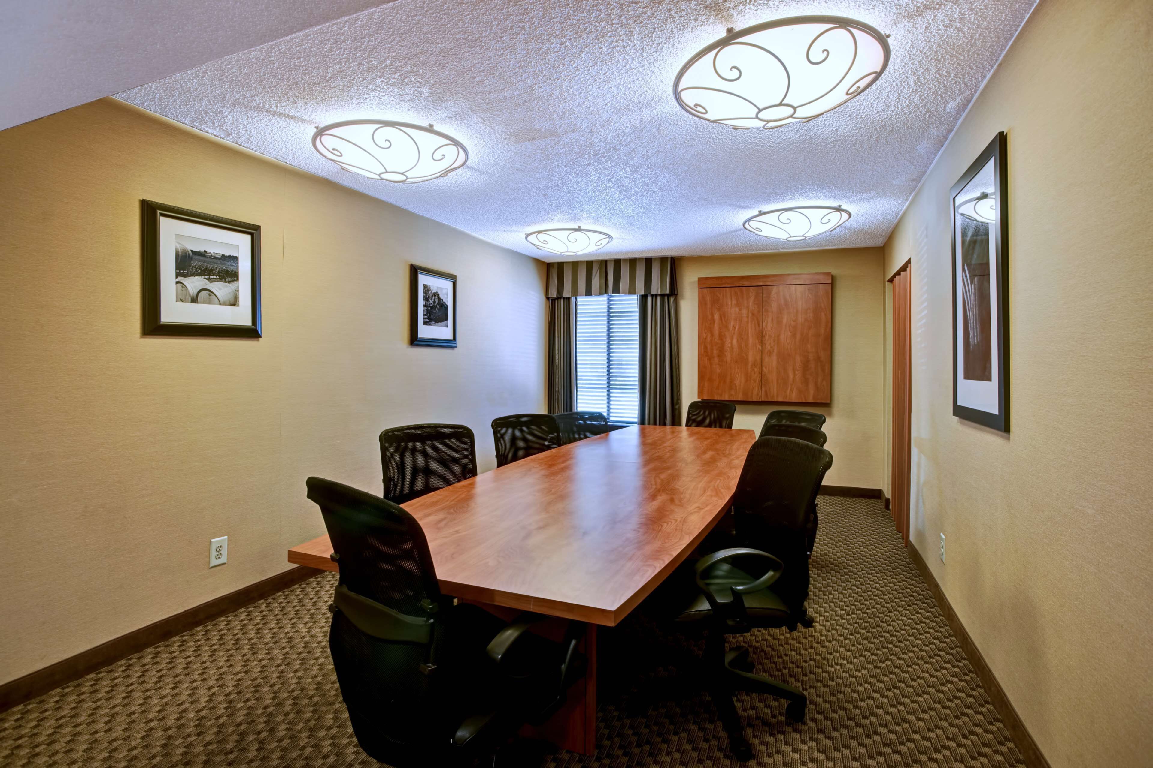 A conference room with a wooden table, black chairs, framed pictures on the walls, and a ceiling with decorative light fixtures.