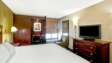 Ein Hotelzimmer mit einem großen Bett, einem Schreibtisch, einem Sessel, einem Fernseher und einem Schminktisch.