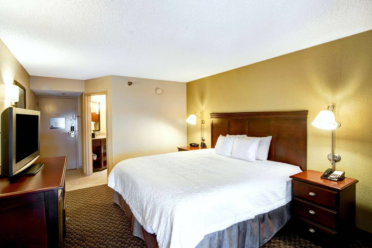 A hotel room with a large bed, bedside lamps, a TV, and a desk.