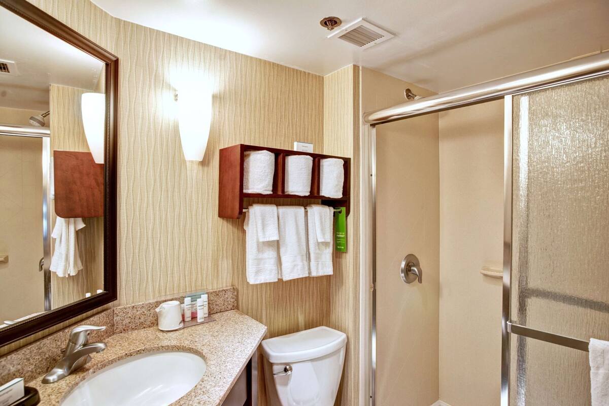 A bathroom with two sinks, a toilet, a shower, and a towel rack with towels.