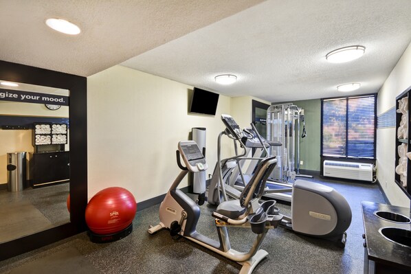 Une salle de sport équipée de machines de cardio, d’un ballon d’exercice rouge et d’une horloge murale.