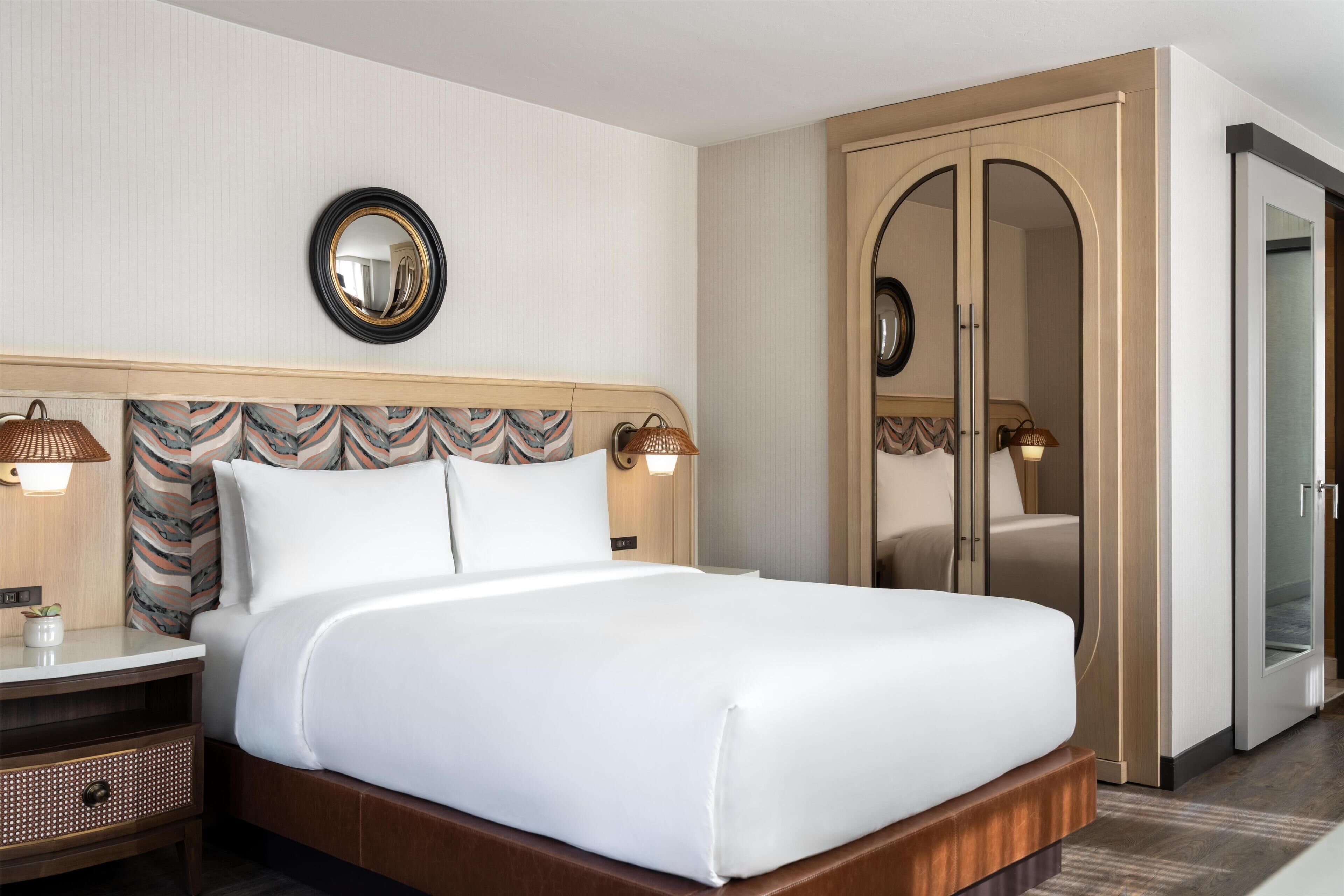 Una habitación de hotel con una cama grande, una mesita de noche, un espejo, un armario y una puerta.