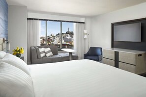 Une chambre d’hôtel avec un grand lit, un canapé, une petite table, une télévision et une vue sur la ville.