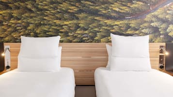 A room with two beds, a wooden headboard, and a wall mural of trees.