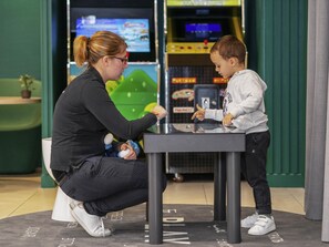 A woman and a child playing a video game at a table in a room with arcade machines in the background.