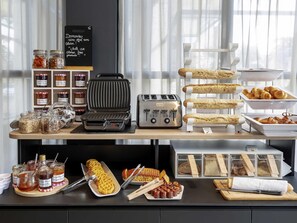 Ein Frühstücksbuffet mit verschiedenen Speisen, einem Waffeleisen und einem Toaster.