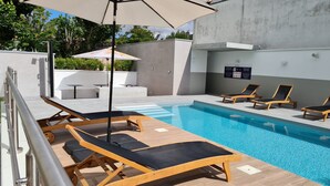 A modern outdoor pool area with wooden loungers and a covered seating area.