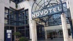 A hotel entrance with a glass facade, a sign reading 'NOVOTEL,' and a tiled pavement.