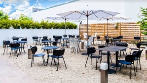 An outdoor patio with multiple tables and chairs, umbrellas, and a wooden fence.