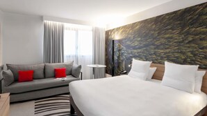 A hotel room with a bed, a sofa, a small table, and a wall with a nature-themed mural.