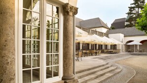 A building with large windows, outdoor seating area with umbrellas, and stone steps leading to the entrance. - Ramada by Wyndham Nuernberg Parkhotel (Nuremberg)