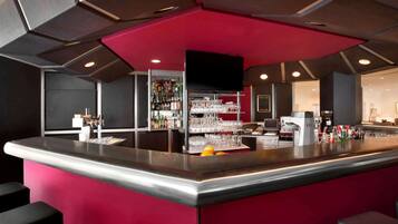 A bar area with a red accent wall, shelves with glasses and bottles, and a flat-screen TV mounted on the wall.