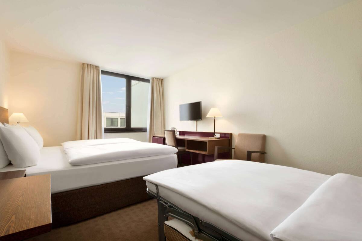 Une chambre d’hôtel avec deux lits, un bureau, une chaise, une télévision et une fenêtre avec des rideaux.