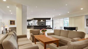 A modern hotel lobby with a sofa set, a wooden coffee table, and a piano. - Ramada by Wyndham Nuernberg Parkhotel (Nuremberg)