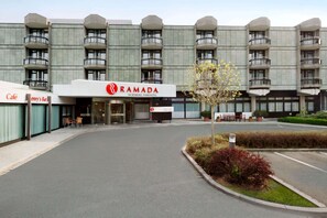 Een modern gebouw met een bordje voor Ramada Nurnberg Parkhotel, met een gebogen entree, een terras en een aangelegde tuin.