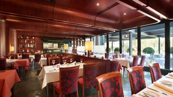 A restaurant with wooden paneling, tables with white tablecloths, and chairs with red floral upholstery.