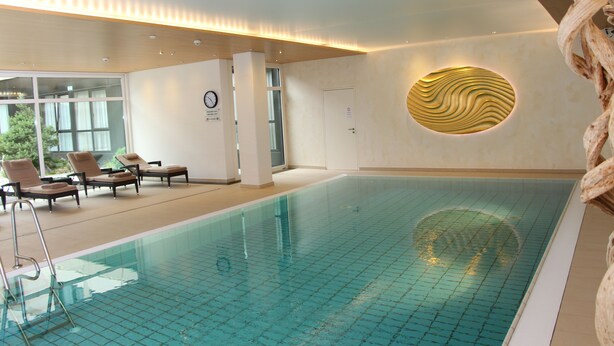 An indoor swimming pool with lounge chairs, a clock, and a unique wall design. - Ramada by Wyndham Nuernberg Parkhotel (Nuremberg)