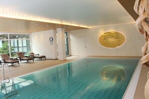 Una piscina interior con sillones de descanso, un reloj y un diseño de pared singular.