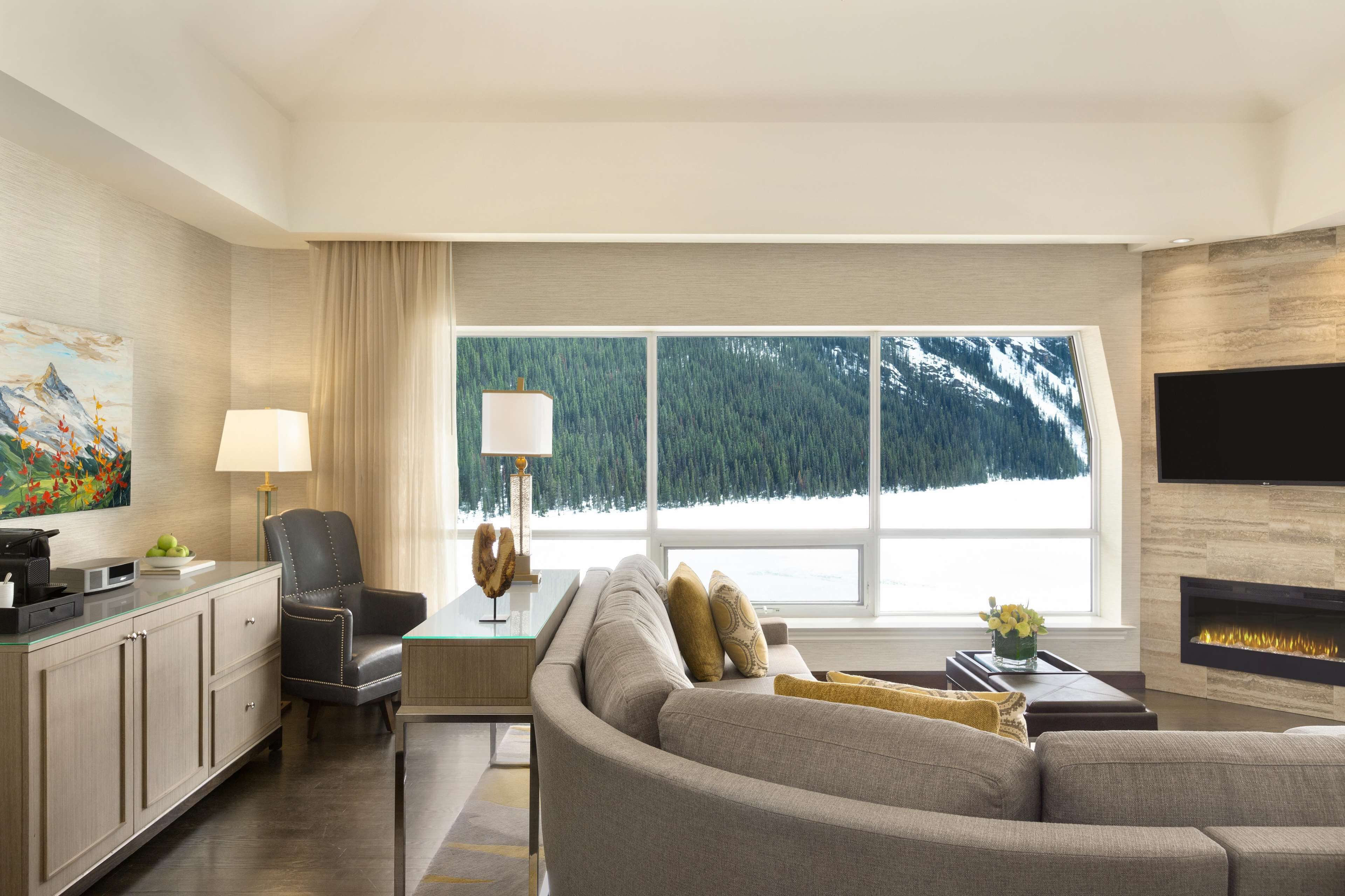 A modern living room with a large window, a fireplace, and a flat-screen TV mounted on the wall.