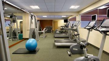 Un gimnasio con equipamiento de ejercicio, una pelota de ejercicio azul grande y una cinta de correr.