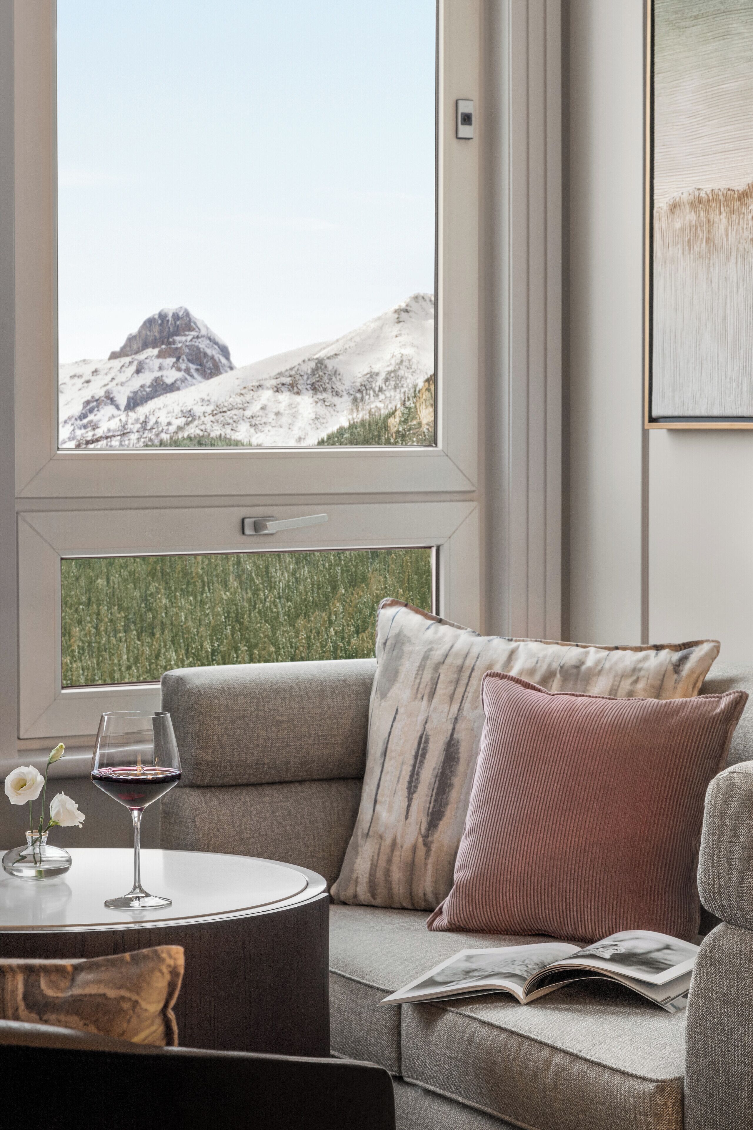 A modern living room with a large window, a grey sofa, a round coffee table, and a wine glass.