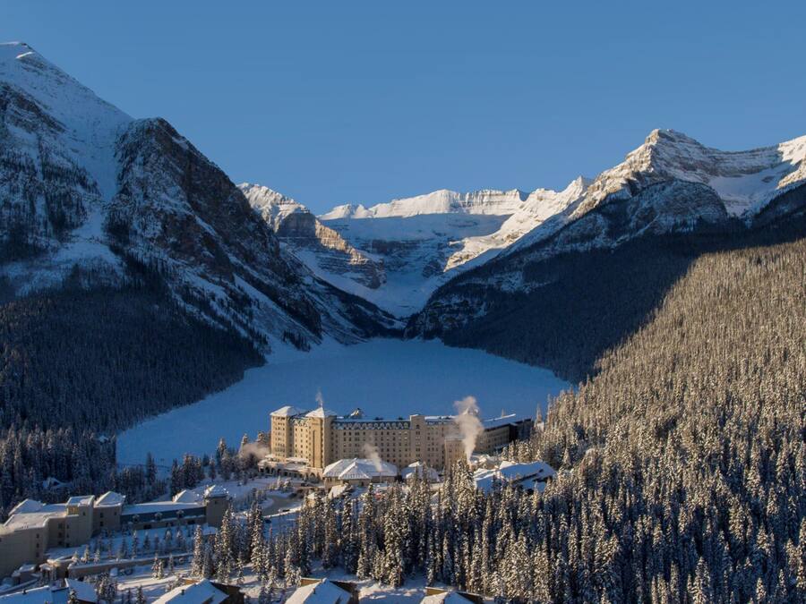 A snow-covered mountain landscape with a large building in the foreground, surrounded by dense forests and snow-covered peaks.