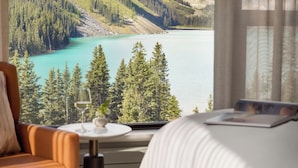 Ein Schlafzimmer mit Blick auf einen türkisblauen See, umgeben von bewaldeten Bergen.