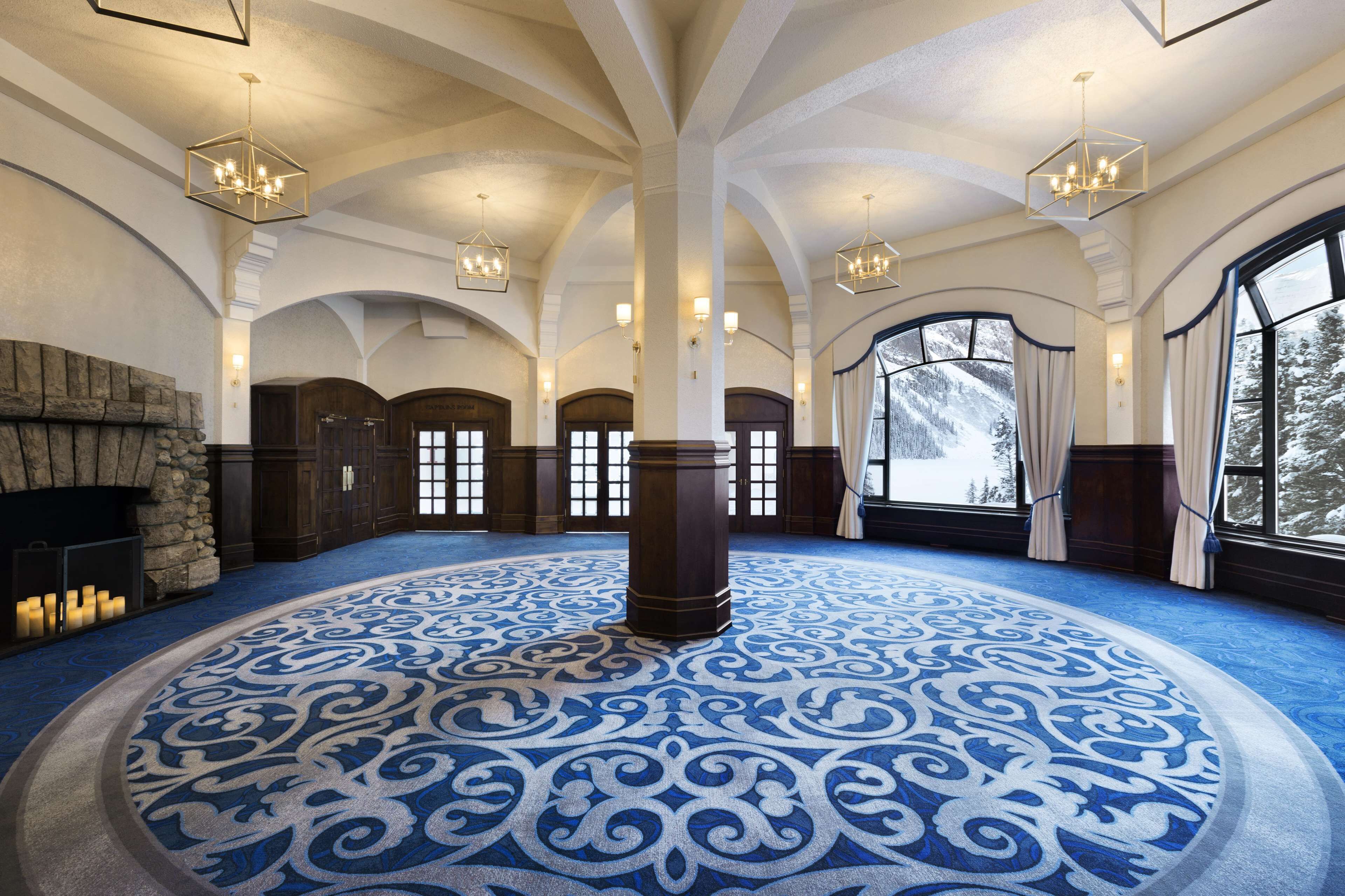 Eine großzügige Lobby mit einem gemusterten Teppich, einem Kamin aus Stein und großen Fenstern mit Blick auf schneebedeckte Bäume.
