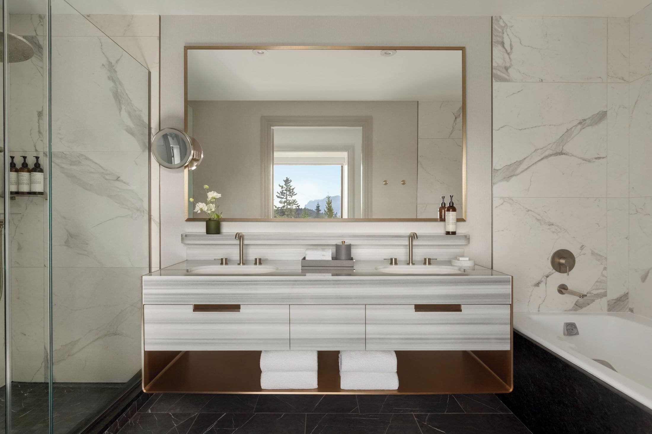A modern bathroom with a large mirror, dual sinks, and a bathtub.