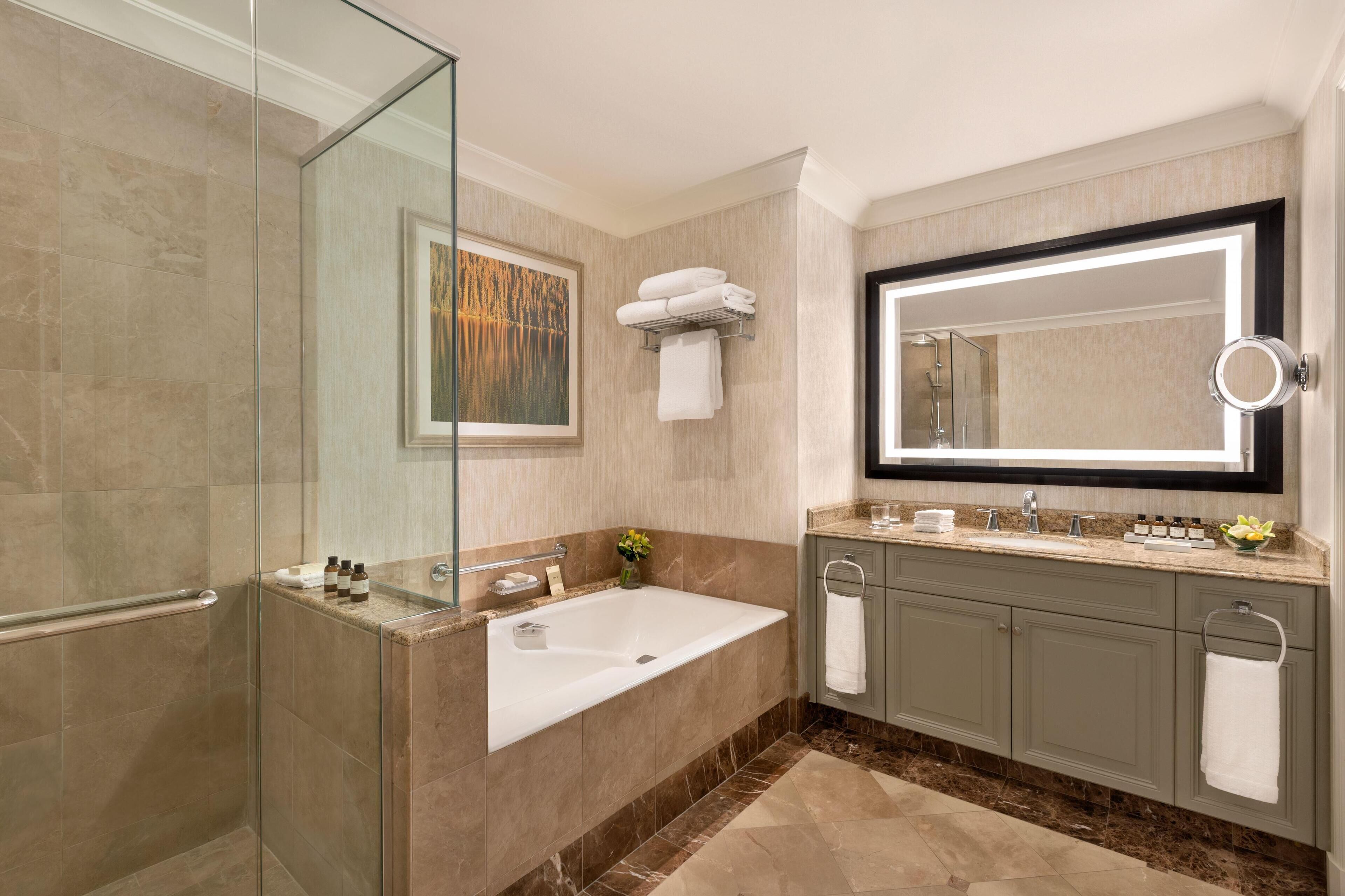 Un baño moderno con cabina de ducha de vidrio, una bañera grande, un tocador con espejo y suelo de mármol.