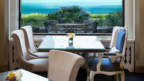Ein Essbereich mit Tisch und Stühlen, ein Fenster mit Blick auf Berge und See, und eine Vase mit Blumen auf dem Tisch.