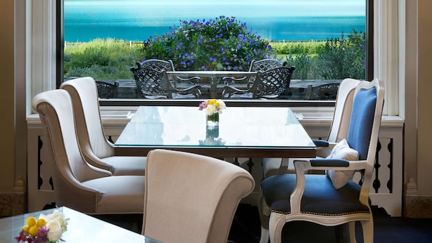 Ein Essbereich mit Tisch und Stühlen, ein Fenster mit Blick auf Berge und See, und eine Vase mit Blumen auf dem Tisch.