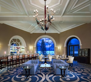 A spacious lobby with a grand chandelier, multiple seating areas, and large windows offering a view of the outdoors.