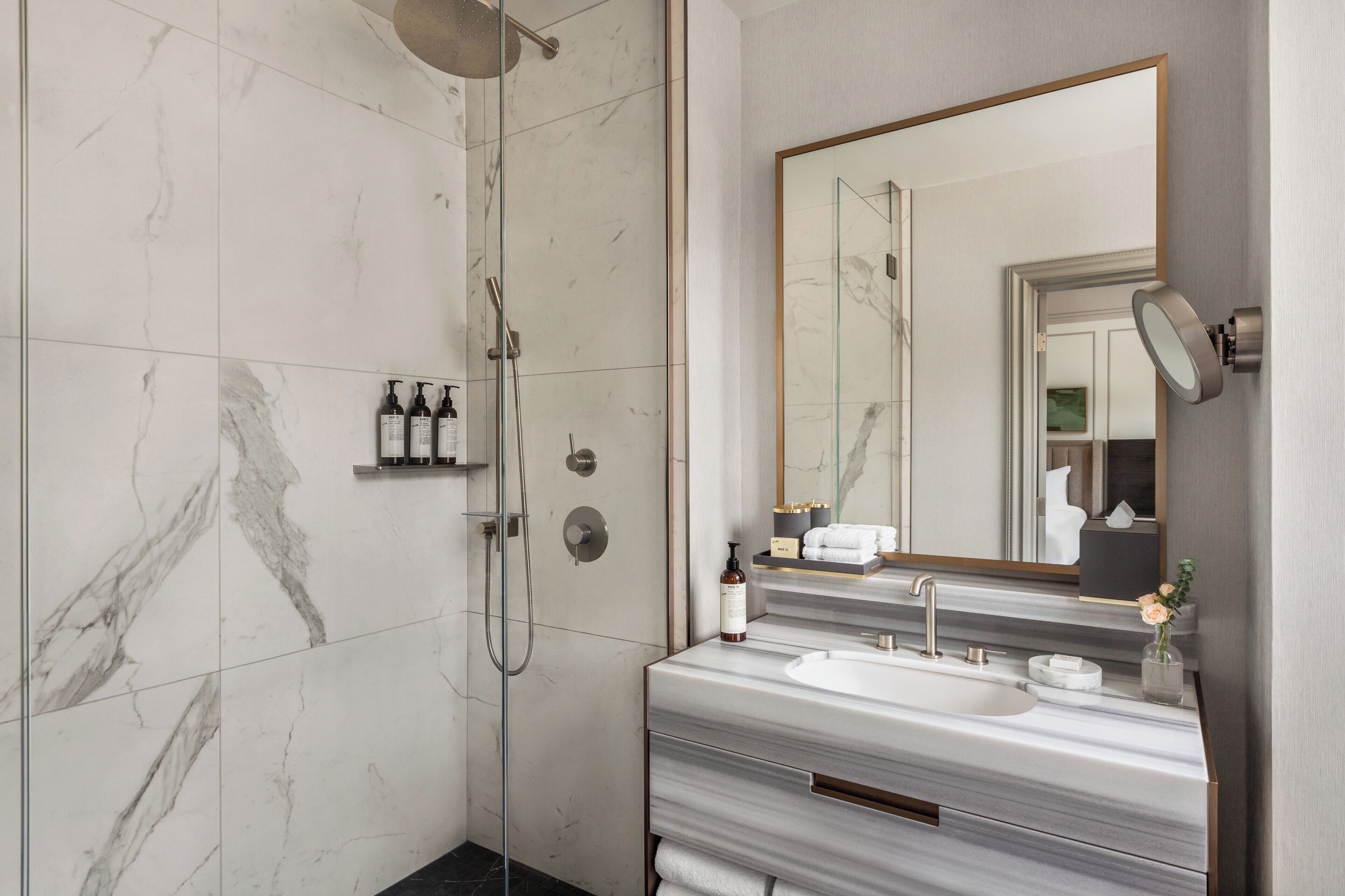 A modern bathroom with a glass-enclosed shower, a marble-tiled floor, a large mirror, and a vanity with a sink and towel rack.