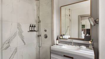 A modern bathroom with a glass-enclosed shower, a marble-tiled floor, a large mirror, and a vanity with a sink and towel rack.