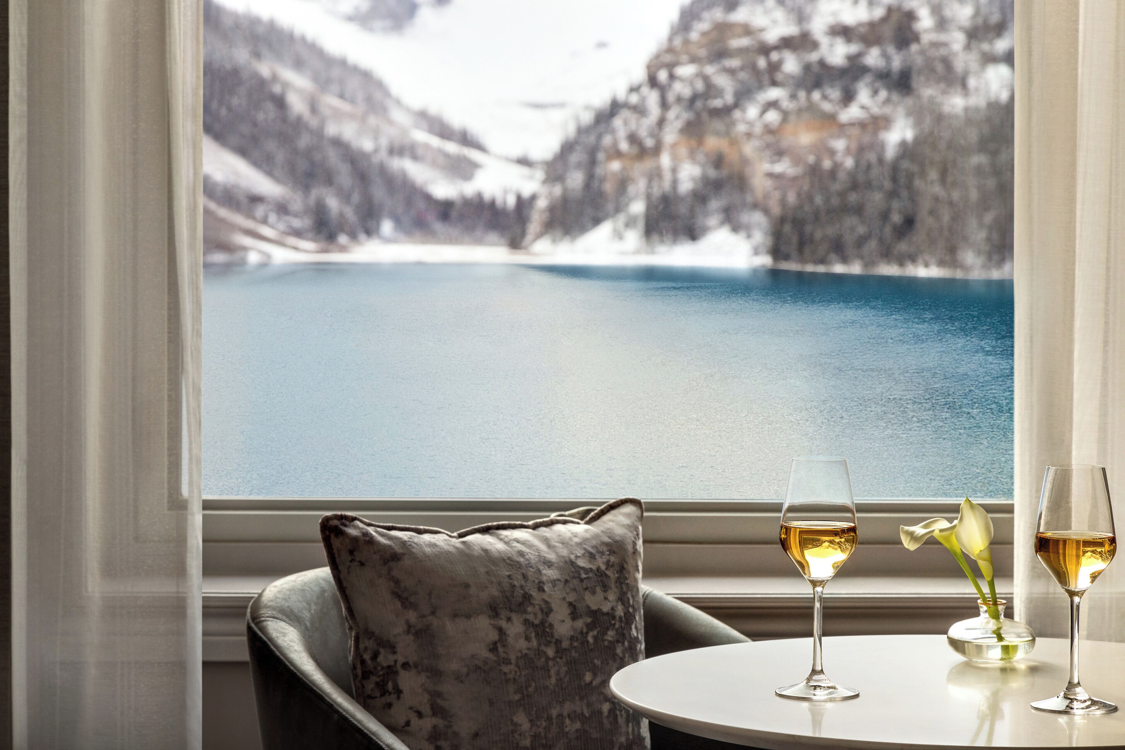 A view of a lake from a window, a table with two glasses of wine, and a cushion.