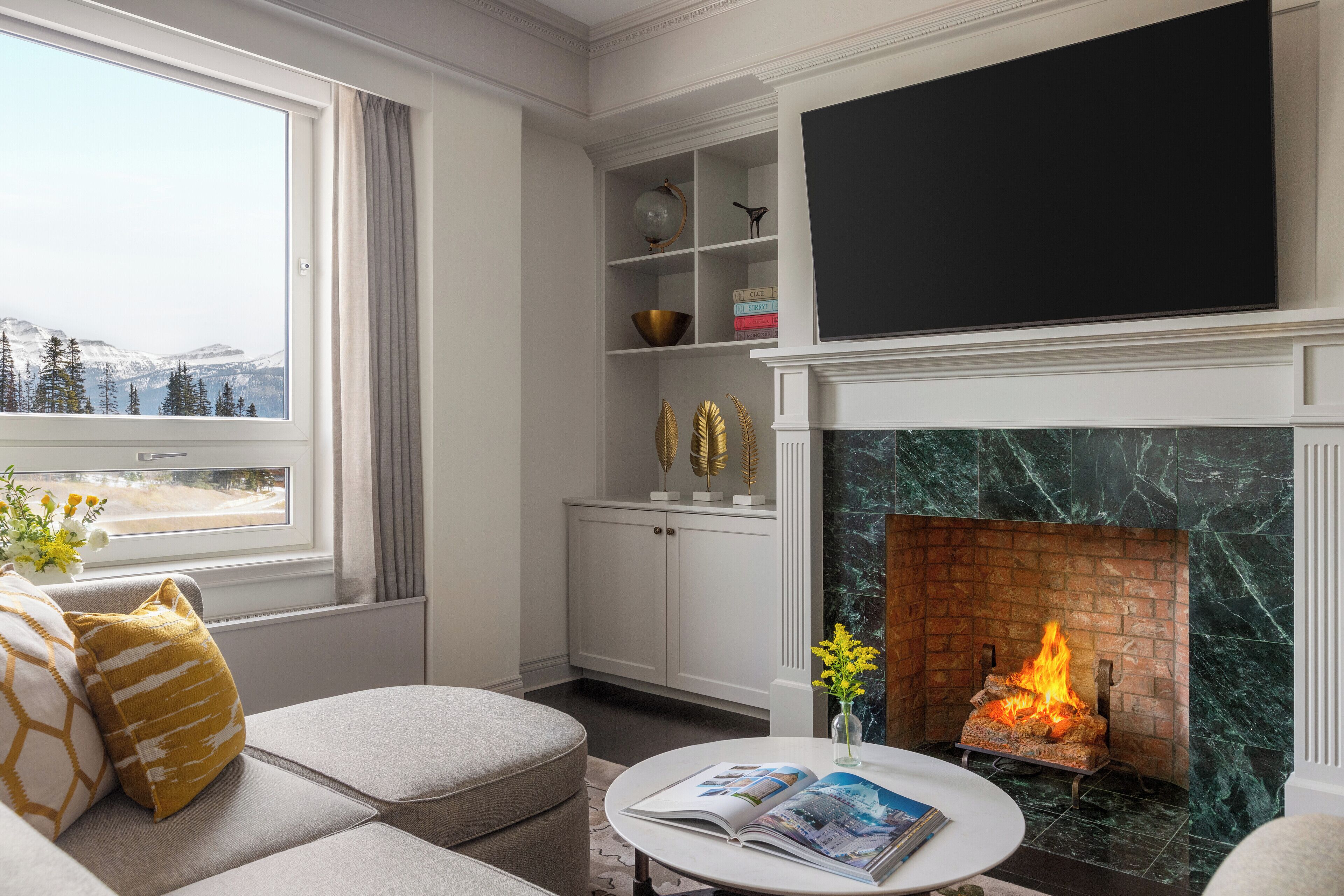 A living room with a fireplace, a television, and a view of snow-capped mountains.