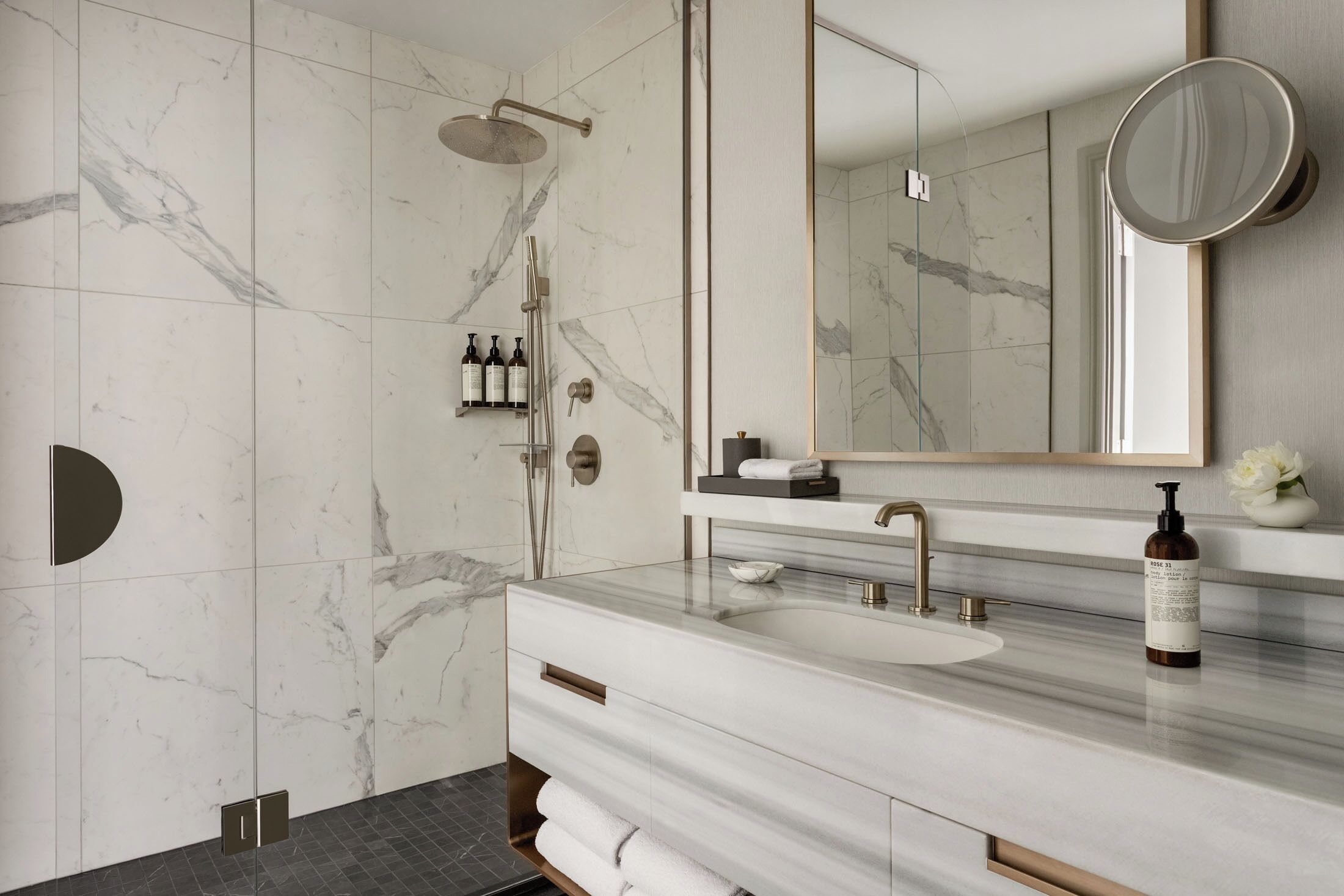 Un bagno moderno con un vanitino in marmo, uno specchio grande e una cabina doccia.