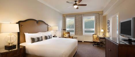 A hotel room with a large bed, a desk with a chair, a television, and a ceiling fan.