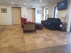 A lobby with a reception desk, a sofa, chairs, and an elevator. - Quality Inn & Suites Ocean City Fenwick (Ocean City)