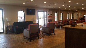 A hotel lobby with a sofa, chairs, a TV, and a dining area with tables and chairs. - Quality Inn & Suites Ocean City Fenwick (Ocean City)